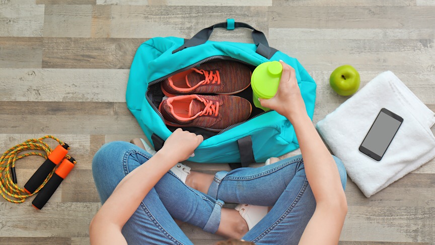 Young woman packing sports bag on floor, top view.