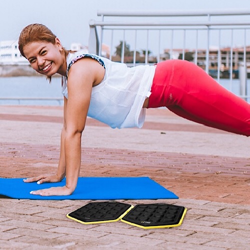 A fit woman doing push ups on a yoga mat beside the slidez-disc.