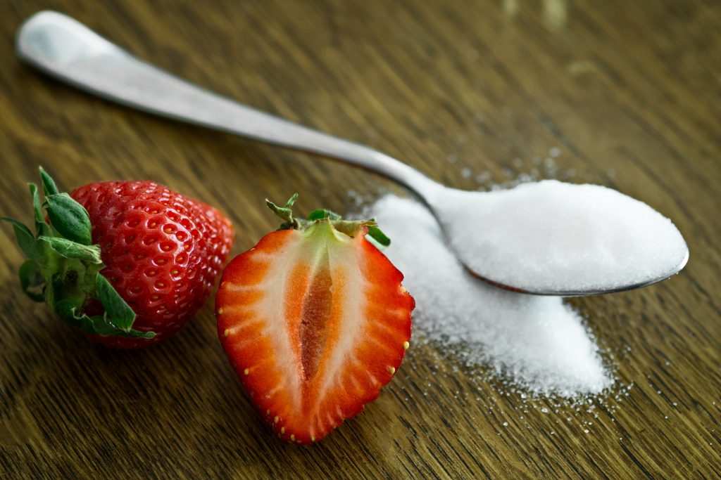 Spoon filled with sugar beside two strawberries. 