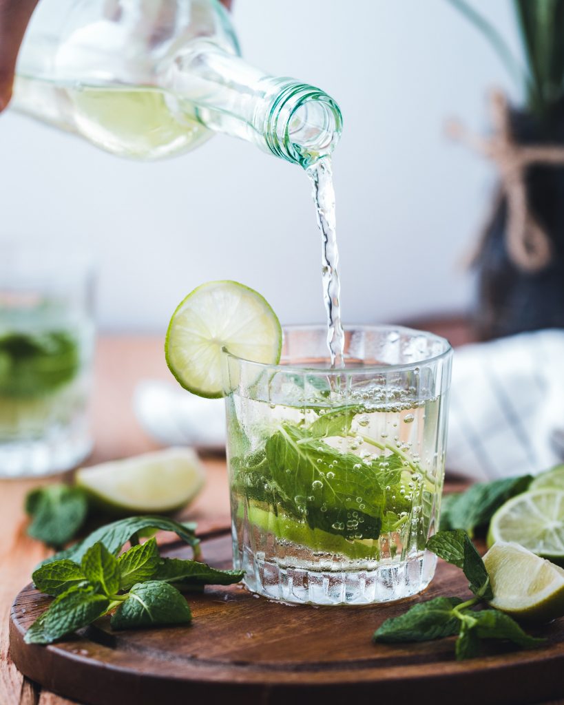 Pouring a drink in a glass with mint leaves and a slice of lime.