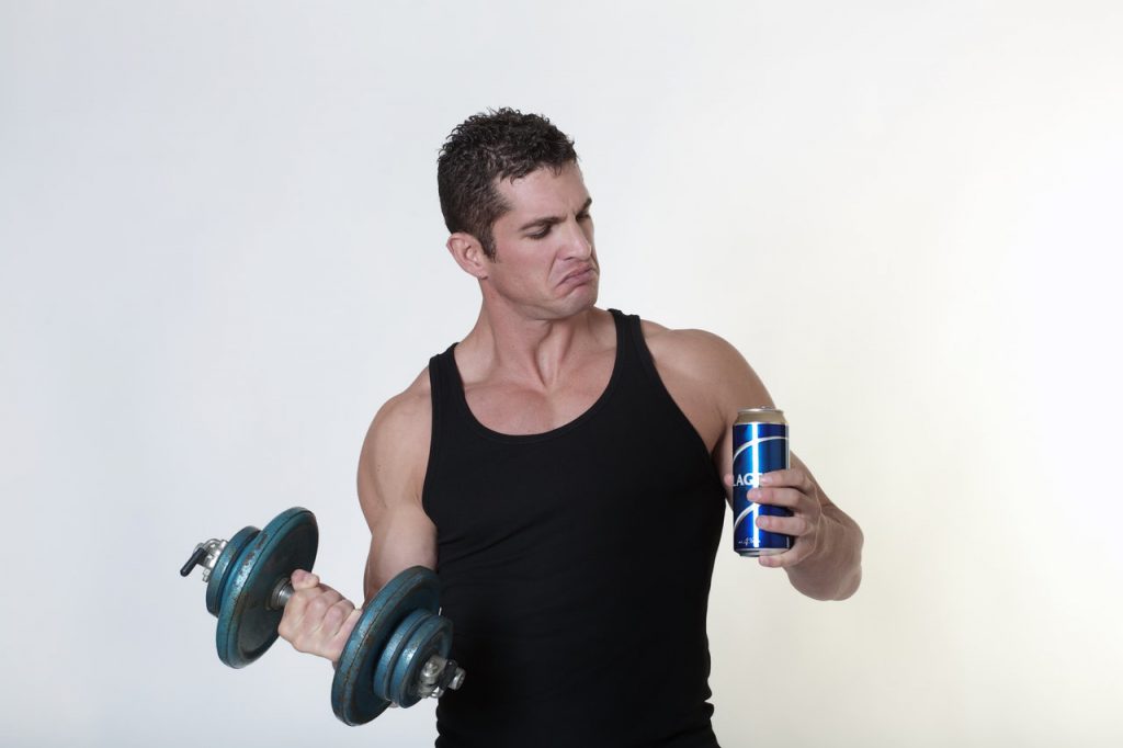 Man holding a dumbbell and a can of beer. Thinking about which one to do between alcohol and workouts.