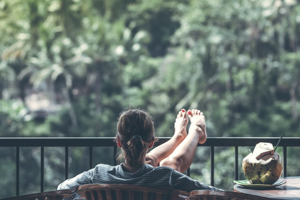 Women sitting on brown chair beside coconut drink, feeling relaxed which is one of the effects of Onnit New Mood Supplement.