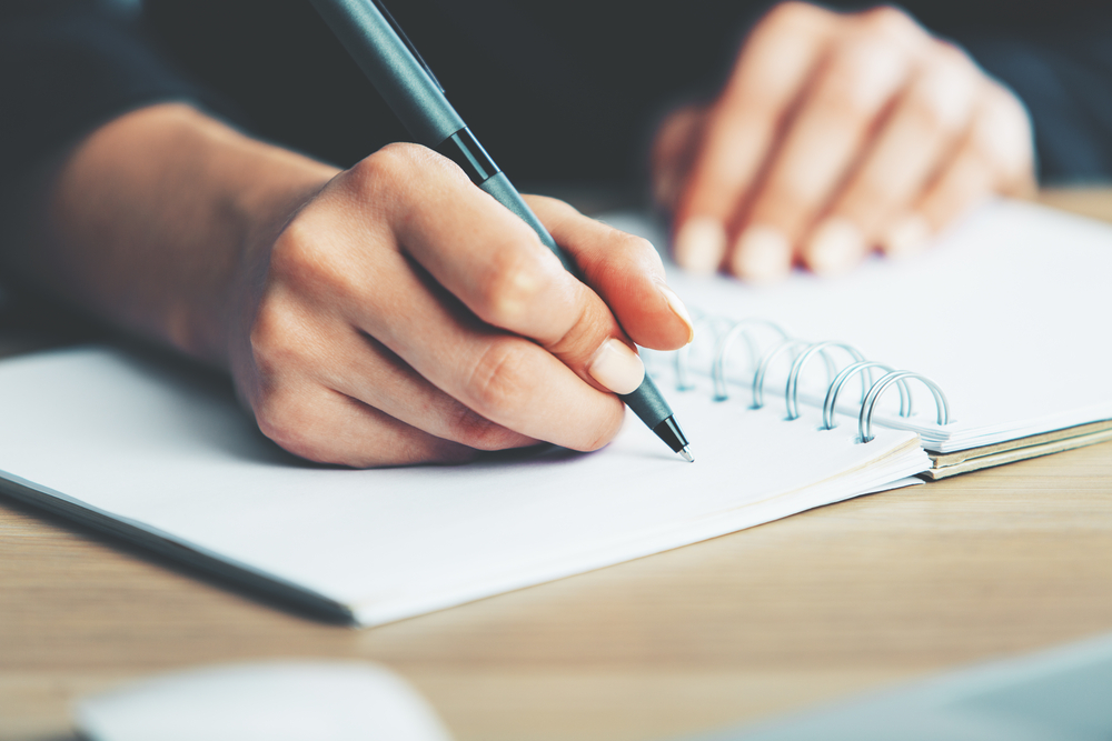 Close up of man writing in notebook. Keeping a food diary is one of the healthy hacks for nutrition and fat loss.