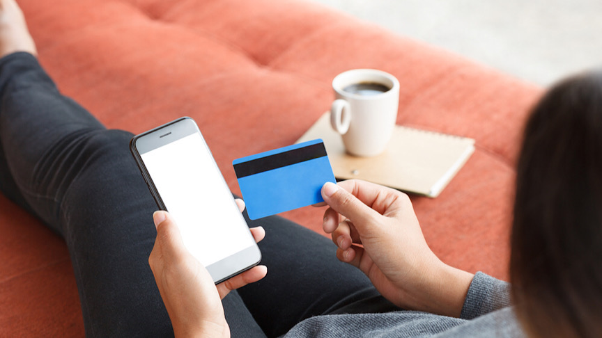 Woman holding iphone next to credit card.