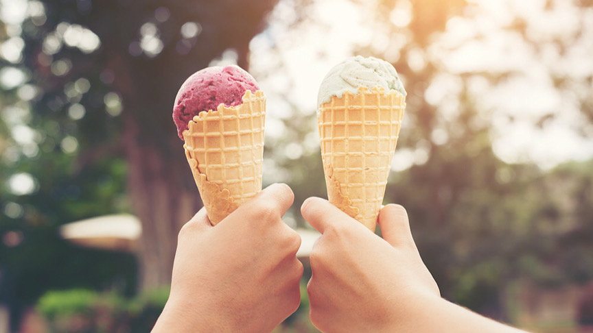 Woman's hands holding melting ice cream waffle cone in hands on summer light nature background