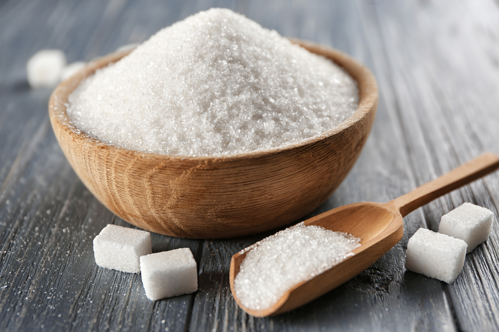 Bowl and scoop with white sand and lump sugar on wooden background