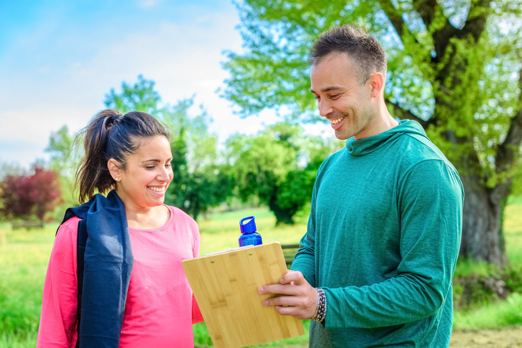 A young woman talking to her personal trainer about her fitness goals and achievements.