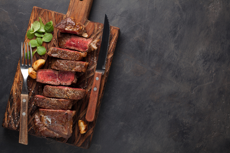 Closeup ready to eat steak new York beef breeds of black Angus with herbs, garlic and butter on a wooden board.