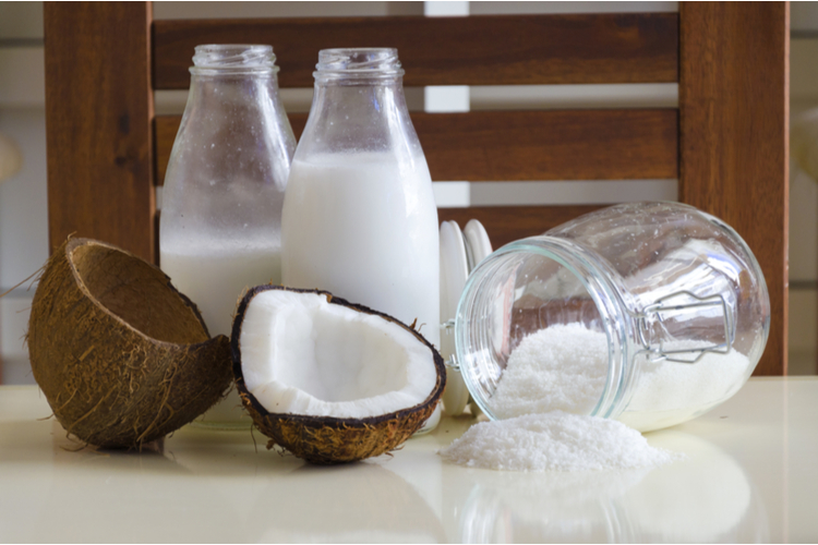 Cracked open coconut with meat cut in half, grounded flakes in a mason jar.