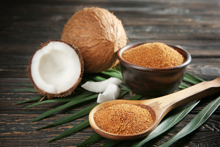 Bowl and spoon of brown sugar with coconut on wooden background.