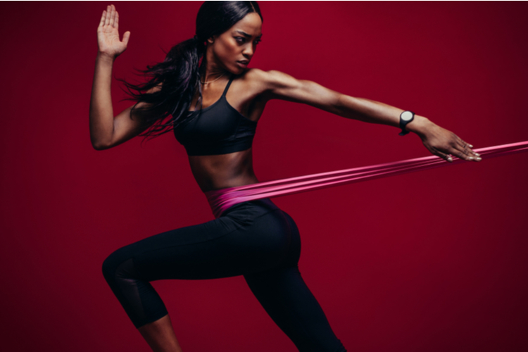 Strong woman using a resistance band in her exercise routine. Female athlete exercising with resistance band in studio.
