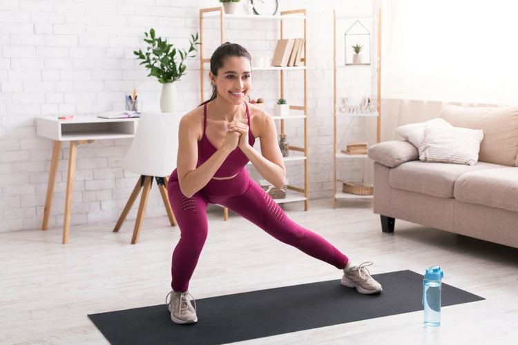 Happy millennial girl doing lunges on yoga mat following the FIIT formula in light room.