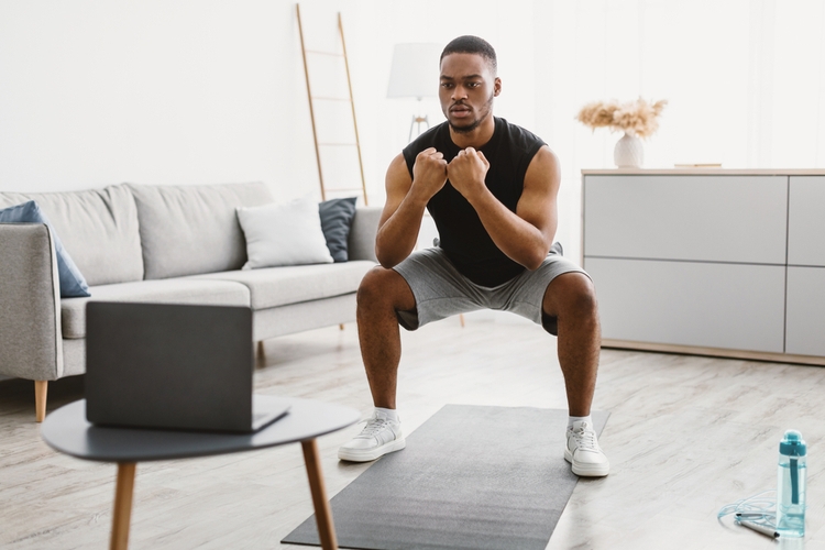 Man doing deep squats looking at laptop.