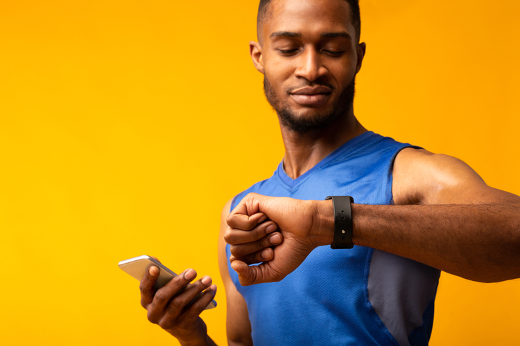 Muscular man looking at smartwatch while holding smartphone.