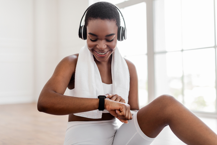 Woman looking at activity fitness tracker smartwatch during workout break to play spotify.