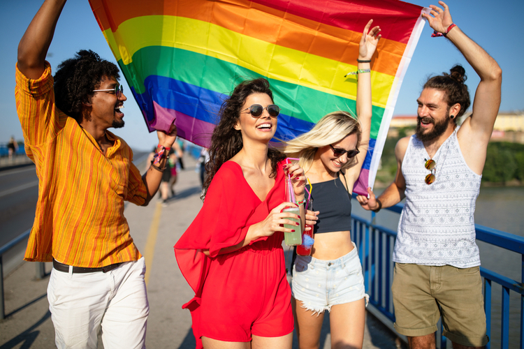 Group of friends in a community at a parade with hands raised and the LGBT flag.