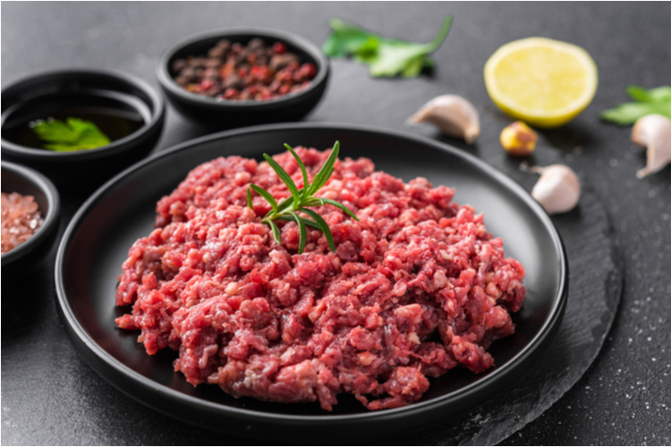 Ground beef on a black plate against stone background.