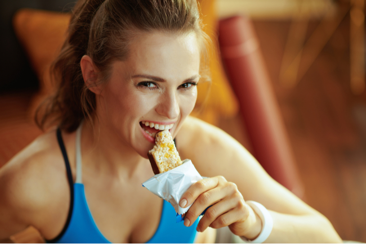 Woman eating carrot cake protein bar before workout session.