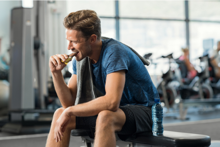 Sweaty young man eating energy bar at gym.