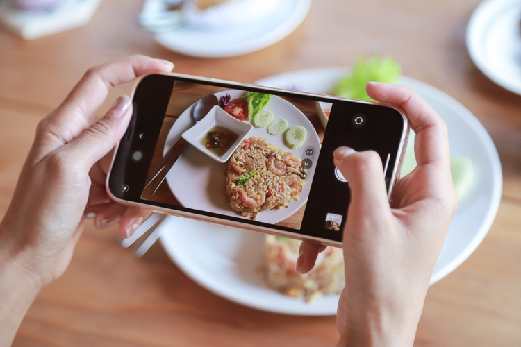 Hand hold smartphone taking photo of fried rice on dish before eating in cafe. 