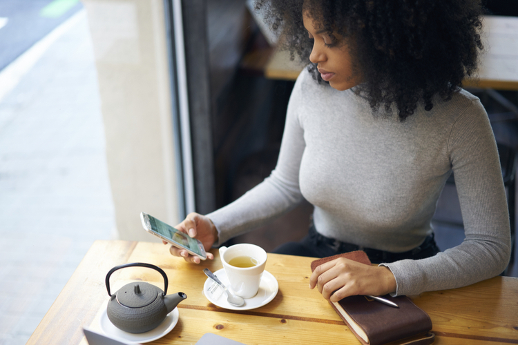 Woman sitting in a cafeteria tracking her food intake via a food journal app.