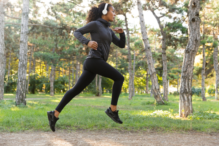 Image of feminine woman adidas ultimafusion and headphones working out while running through green park.