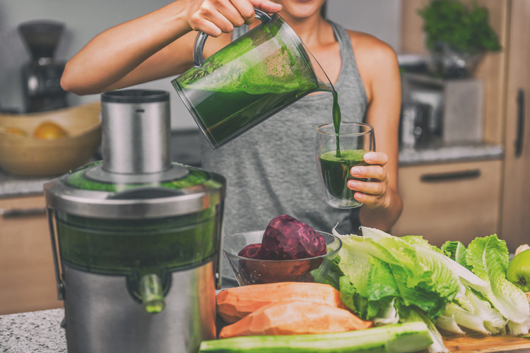 Woman juicing making green juice with juice machine in home kitchen.