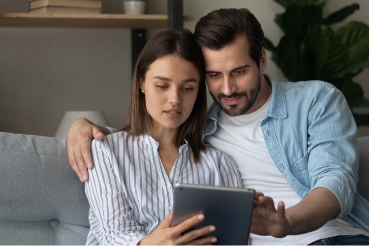 Focused married couple read insurance policy loan contract text from bank website on tablet.