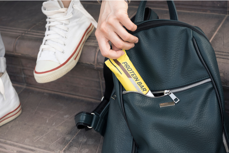 Close-up of a Girl Crouched On The Steps for a Light Snack. She Pulls a Protein Bar Out of Her Women's Backpack