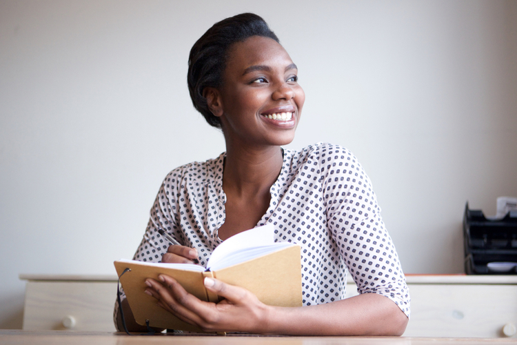 Portrait of smiling young african american woman writing in journal at home
