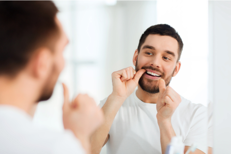 man with dental floss cleaning teeth at bathroom