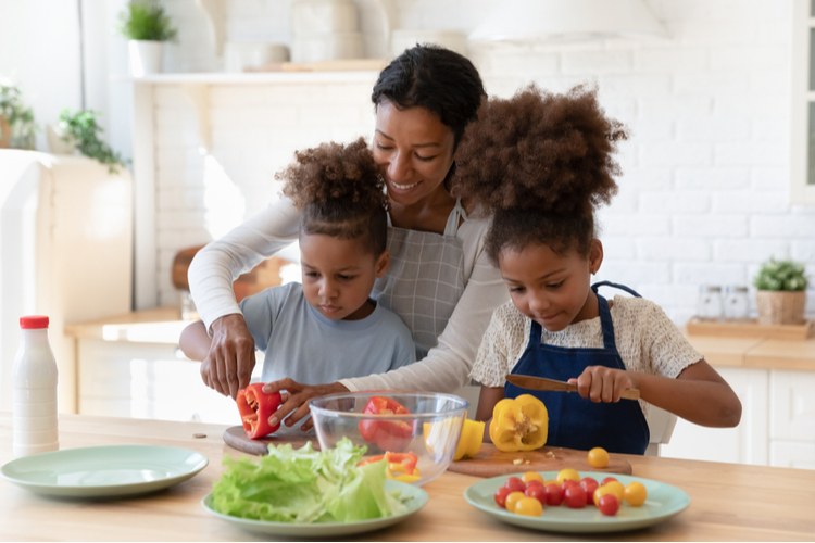 Attentive Patient Smiling African Mom Teaching Explaining Showing Son and Daughter Kids How to Cut Ingredients to Prepare Vegan Salad