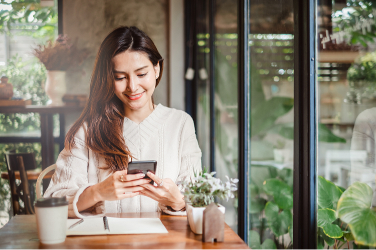 Woman hold phone with notebook by her side to write about money tips