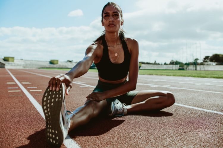 Runner doing stretching exercises sitting on running track.