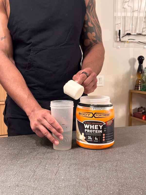 Scooping Body Fortress Whey Protein into a mixer bottle 