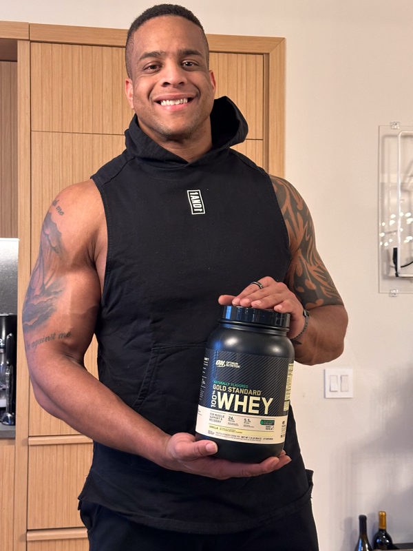 Corey Lewis holding Gold Standard Whey Protein in the kitchen