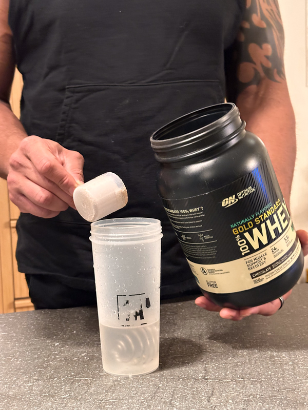 Dumping Gold Standard Whey scoop of protein vanilla into shaker