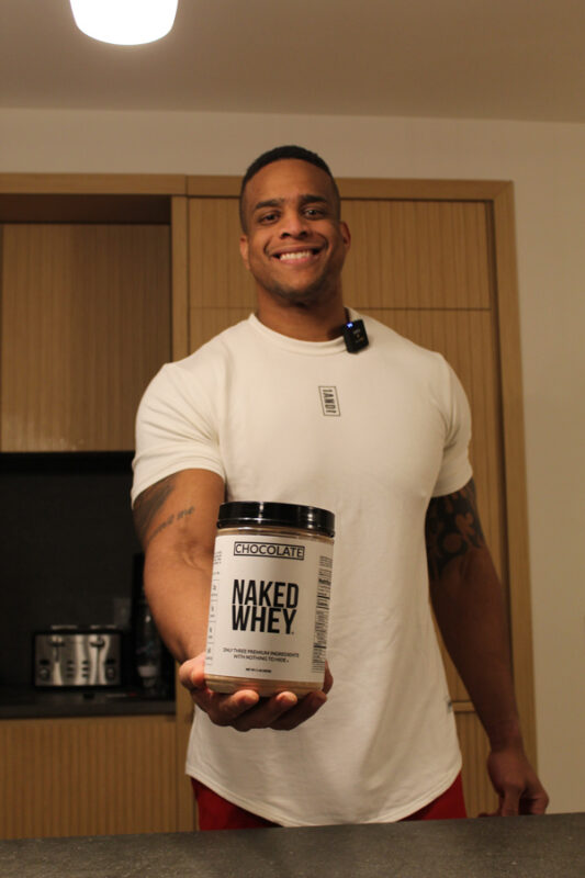 Corey Lewis holding Naked Whey protein in the kitchen 